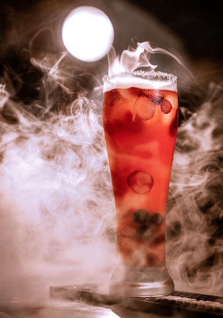 Foto bicchiere di cocktail alcolico rosso su sfondo scuro con fumo e retroilluminazione