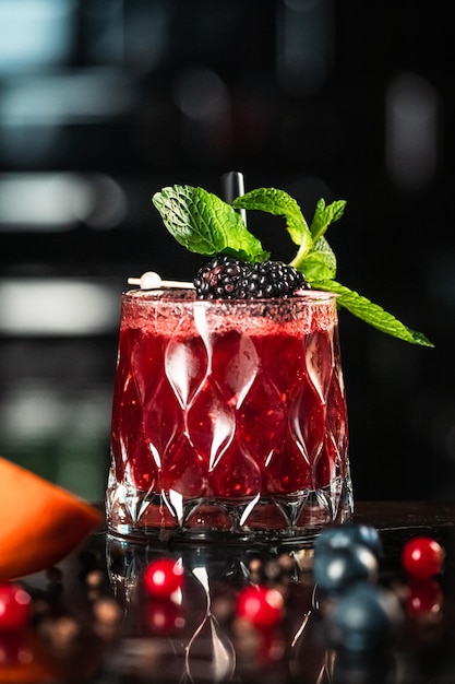 A glass of red cocktail with a black berry garnish