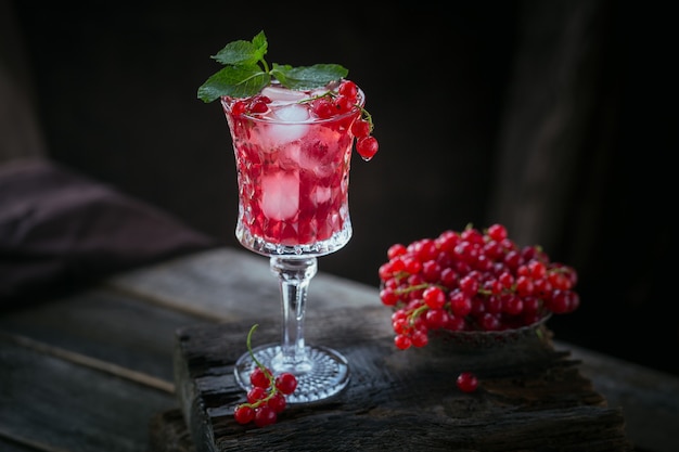 Glass of red currant cocktail or mocktail, refreshing summer drink with crushed ice and sparkling water on a dark wooden surface