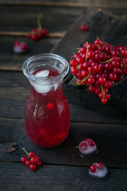 Glass of red currant cocktail or mocktail, refreshing summer drink with crushed ice and sparkling water on a dark wooden