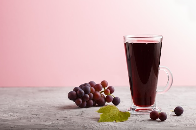 Glass of red grape juice on a gray and pink background. Side view