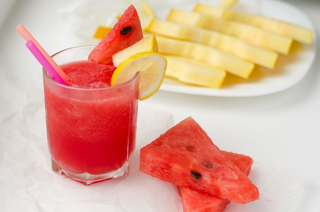 Glass of red watermelon smoothie and slices of melon and watermelon