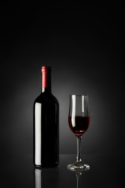 Bicchiere di vino rosso e bottiglia su una parete nera