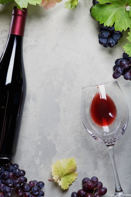 glass of red wine and a bottle of grapes and grape leaves on the table
