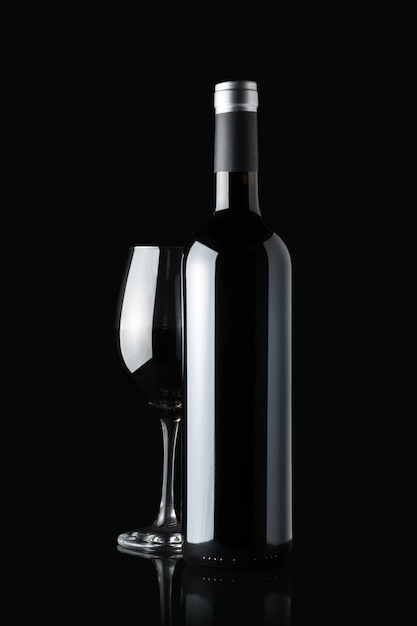 Glass of red wine next to a bottle isolated on black wall