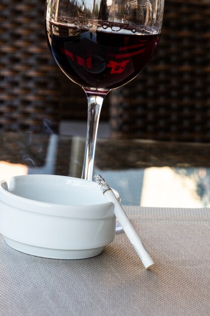 Glass of red wine and cigarette in a white ashtray on the table in a cafe