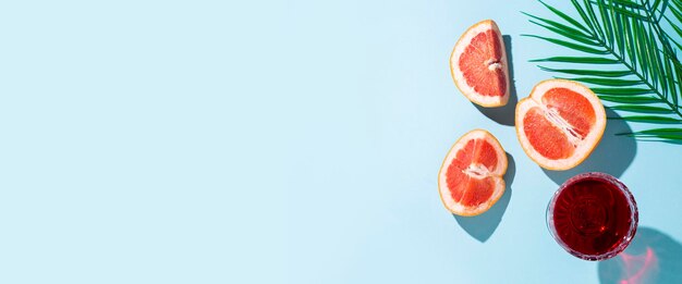 Glass of red wine, cut grapefruit and palm leaf on a blue background. Top view, flat lay. Banner.