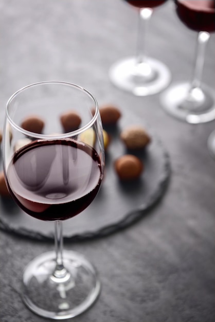 Glass of red wine and delicious chocolate truffles on grey background