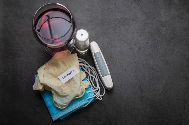 Glass of red wine, face mask , gloves and othe medical objects on dark background