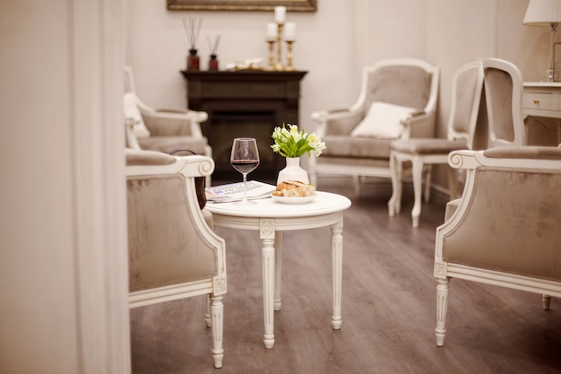 A glass of red wine, fresh pastries and a vase of white flowers sit on the table in the cozy room