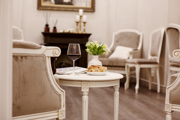 Foto un bicchiere di vino rosso, dolci freschi e un vaso di fiori bianchi siedono sul tavolo nell'accogliente sala