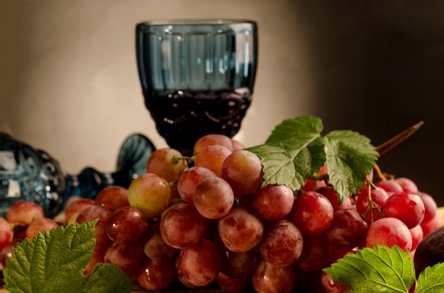 Glass of red wine and Fresh ripe pink grape on a vintage plate, on an old wooden wall.