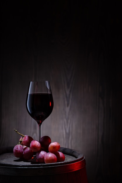 glass of red wine and pink grapes on wooden barrel