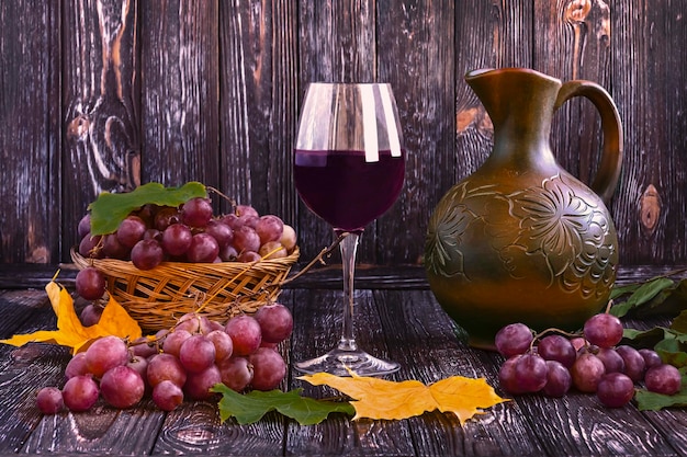 暗い木の背景にストローバスケットのワイン水差しに赤ワインの熟したブドウのグラス