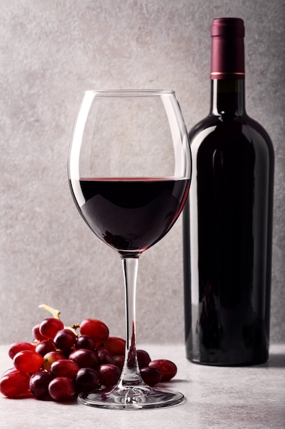 glass of red wine with a bottle and grapes on the table.