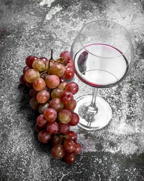 glass of red wine with a branch of fresh grapes. On a rustic background.