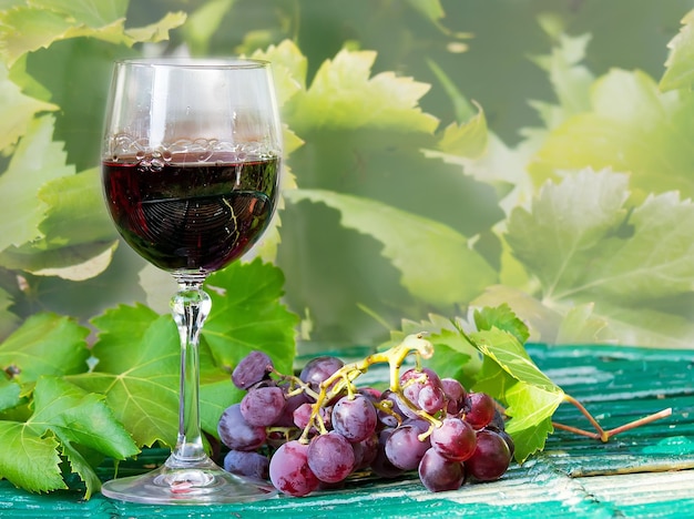 Glass of red wine with grapes and leaves on a wooden table