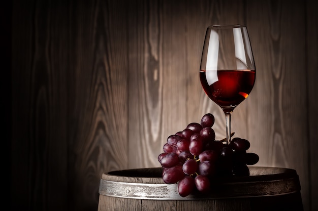 glass of red wine with grapes on wooden barrel