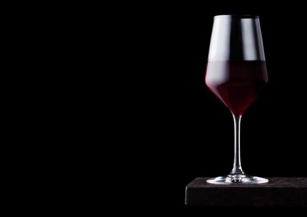 Glass of red wine on wooden board on black table.