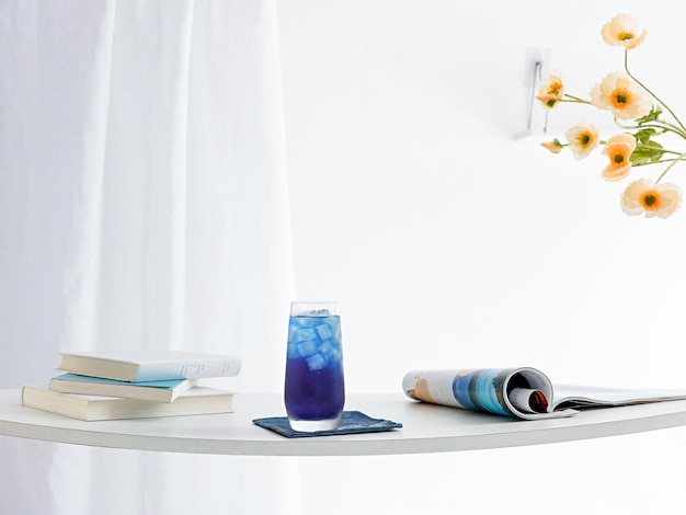 Glass of refreshing blue drink and newspapers on a table with white curtains in the background