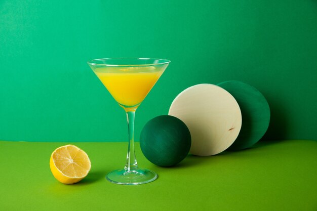 Glass of refreshing citrus cocktail with halved lemon placed on green table with various decorative elements