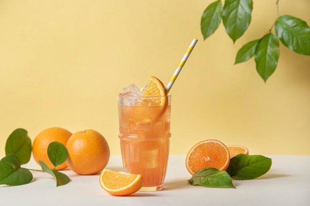 즙이 많은 신선한 과일 오렌지가 있는 노란색 배경에 오렌지 조각과 얼음을 넣은 상쾌한 오렌지 주스 한 잔 탑 뷰 및 복사 공간 이미지