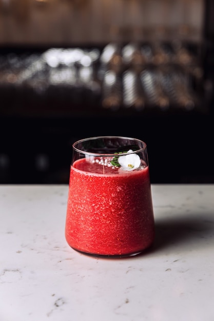 A glass of refreshing strawberry and banana smoothie cocktail garnished with an edible flower, marble table.