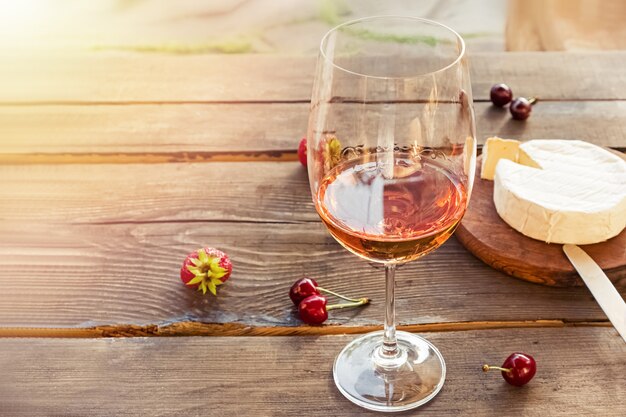 A glass of rose wine standing on rustic wooden table with sunset light effect