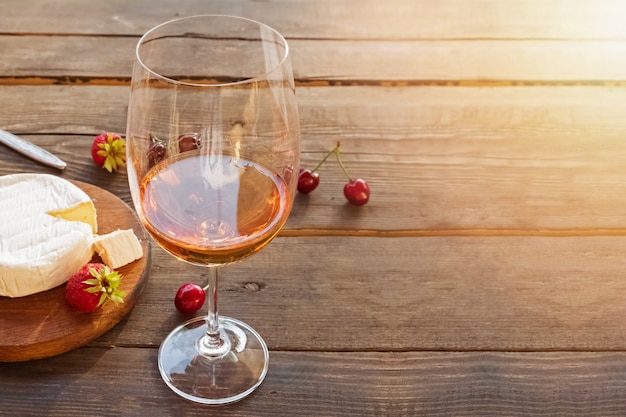 일몰 조명 효과와 소박한 나무 테이블에 서있는 장미 와인 한 잔