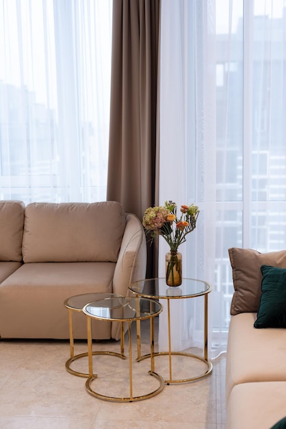 Glass round bedside table with gold with a vase of flowers in a modern beige interior. Interior Design. Soft selective focus, artistic noise.