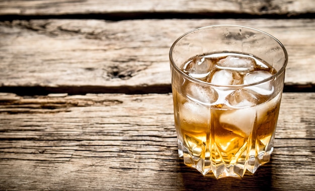 Glass of rum and ice. On wooden background.