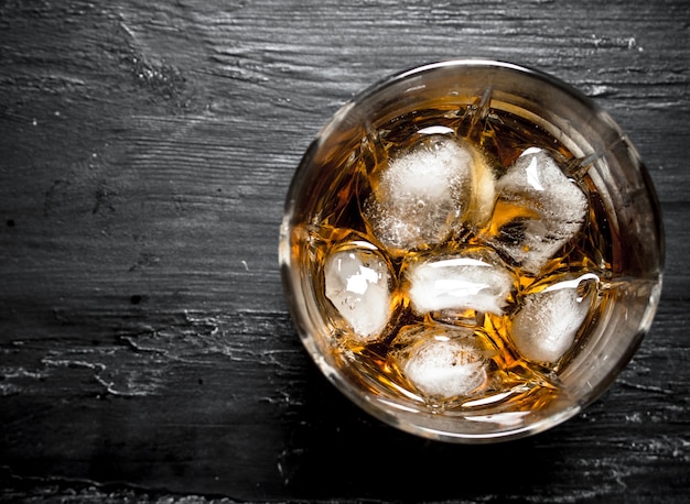 Foto bicchiere di rum con ghiaccio. su uno sfondo di legno nero.