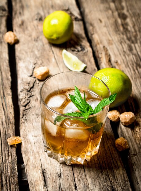 Glass of rum with ice , lime and mint. On wooden background