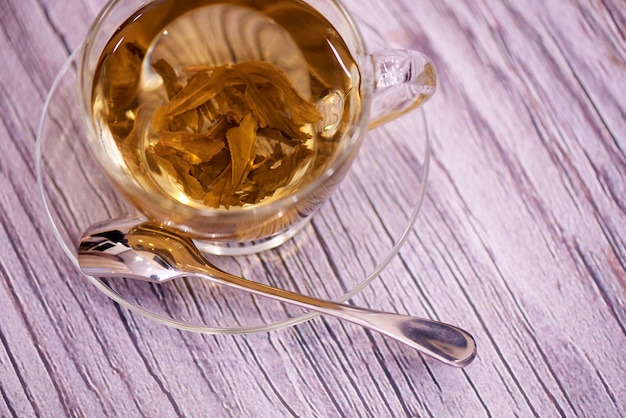 Glass saucer, cup with tea and spoon on wood.