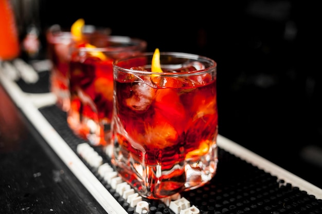 Стакан шотландского виски и лед на фоне красного алкогольного коктейля в баре