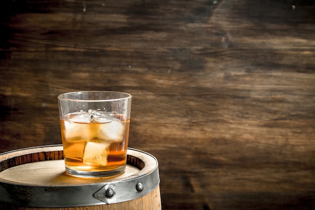 Glass of Scotch whiskey with a barrel. On a wooden background.