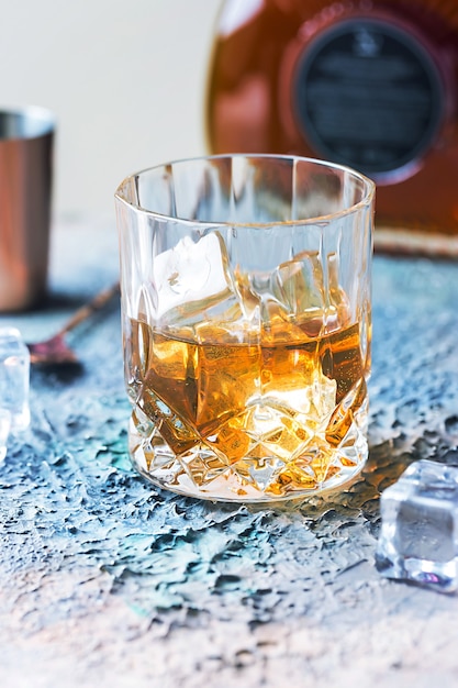 Glass of scotch whiskey with ice cubes, bottle and copper bar accessories