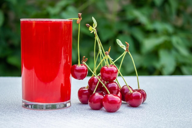 A glass of sour cherry juice on wooden table with cherry fruits.