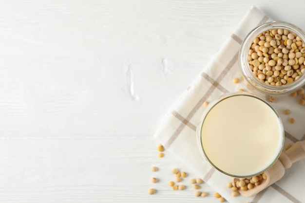 Photo glass of soy milk, soybeats seeds, napkin on white, wood, space for text. top view