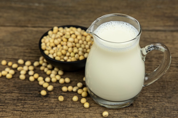 Photo a glass of soymilk with soybeans on wooden table background.