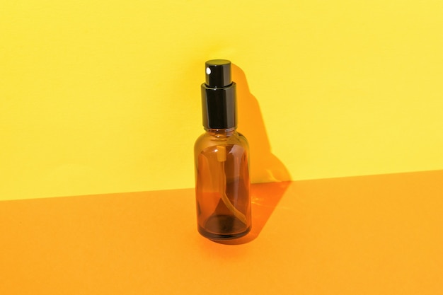 Glass spray bottle in bright light on orange and yellow background. A container for perfumes and cosmetics.