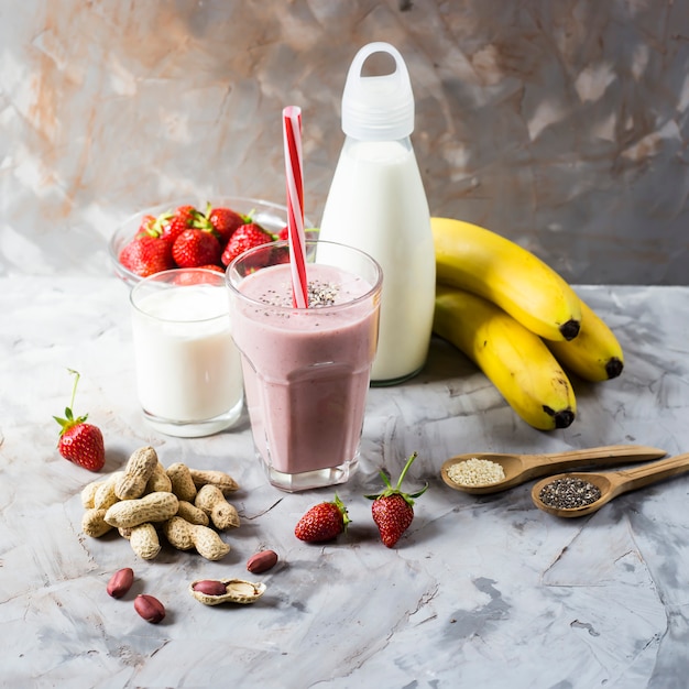 A glass of strawberry-banana smoothie among the ingredients for its preparation