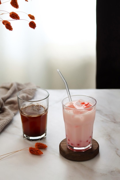 A glass of strawberry milkshake with a red straw next to it.