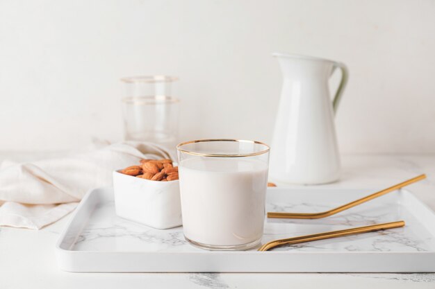 Glass of tasty almond milk and bowl with nuts on light background