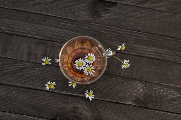 Tazza da tè in vetro con camomilla su una superficie di legno.