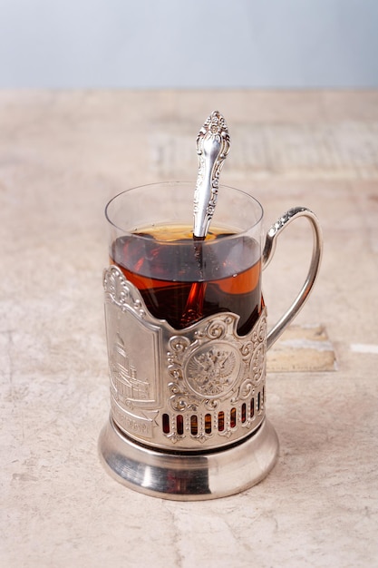 A glass of tea in a metal cup holder on the table