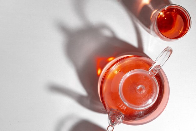 Glass tea pot and glass cup with tea on white backgfround with long shadows