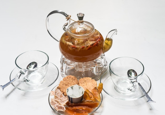 Photo glass tea pot with cups and  crystalized fruits on white background