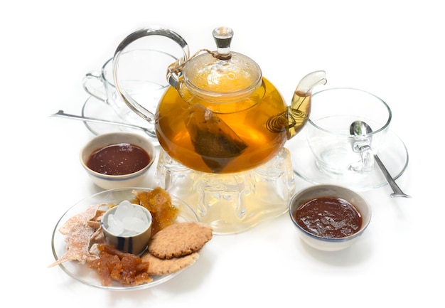 Glass tea pot with cups marmalade and  crystalized fruits on white background