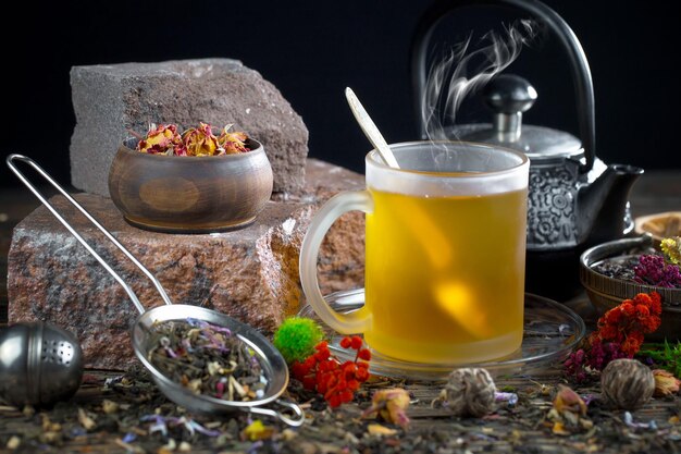 A glass of tea sits on a table with a teapot and a cup of tea.